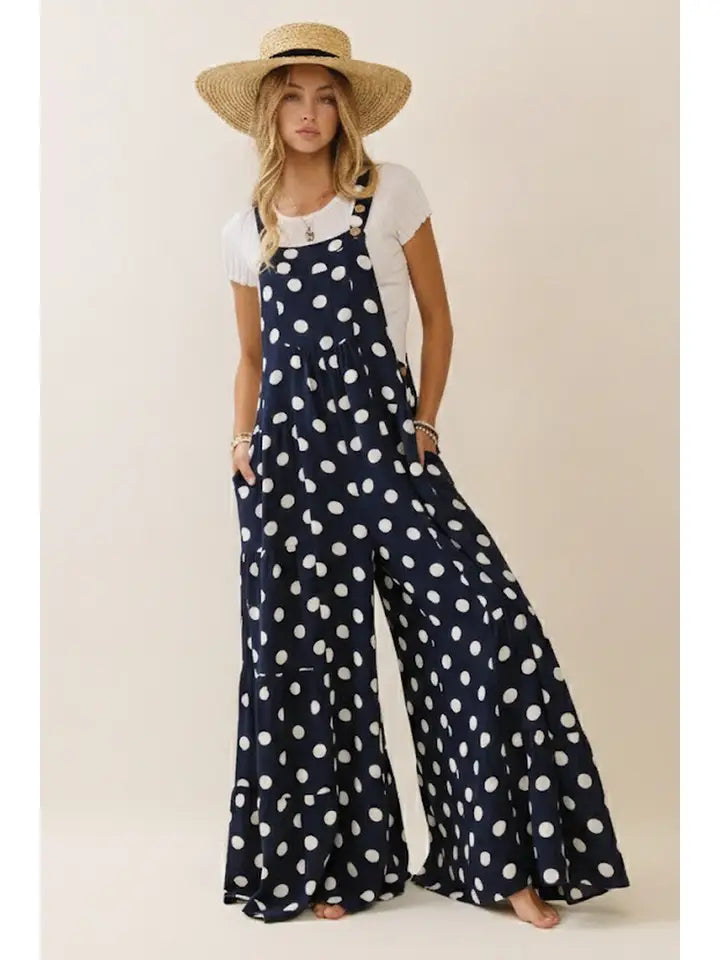 Woman wearing navy polka dot overalls and a straw hat on a plain background