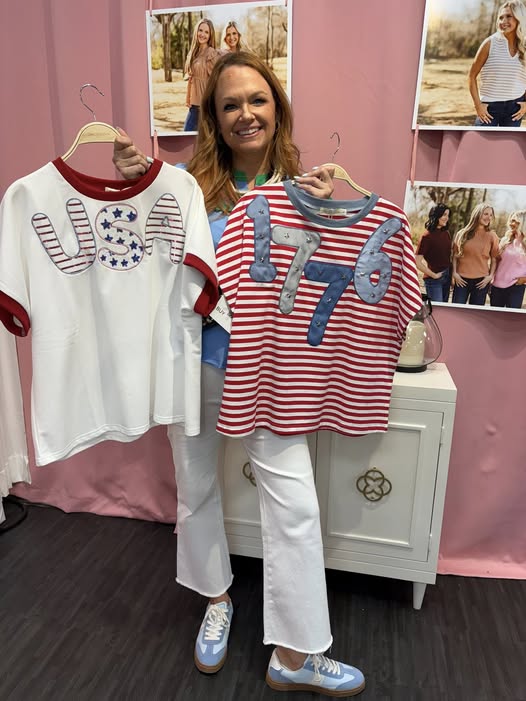 Woman holding two shirts with 'USA' and '1776' designs in a store setting.