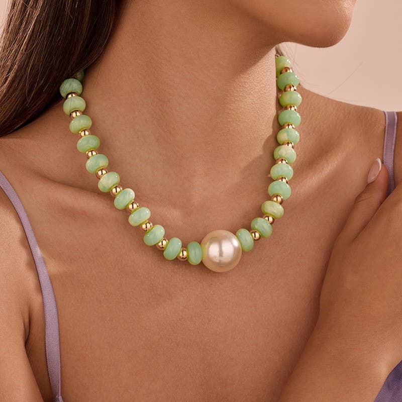 A close-up of a model wearing a necklace made of light green faceted beads separated by small gold spacer beads, with a large round white pearl at the center front.