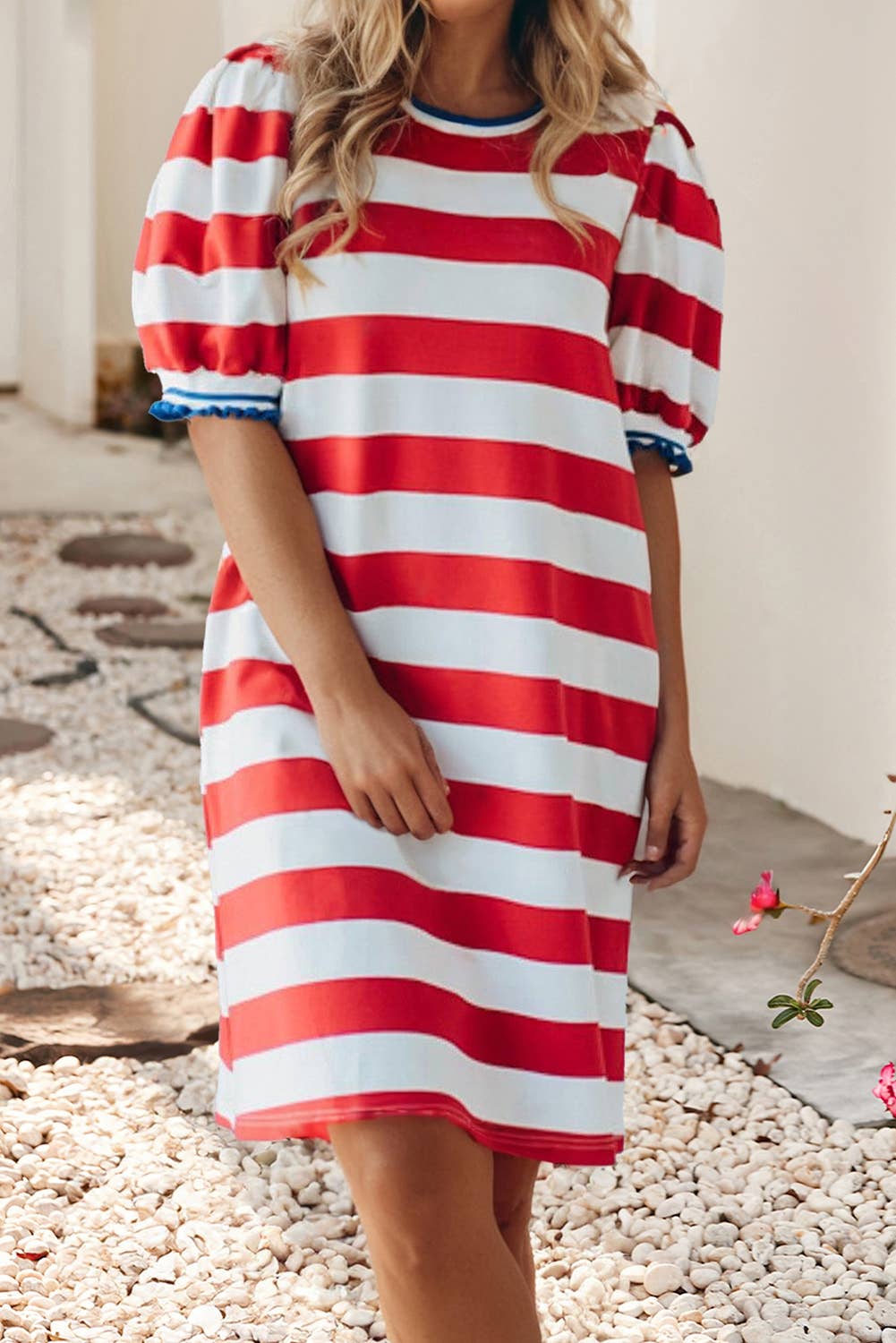 Person wearing a red and white striped dress standing on a pebbled surface.