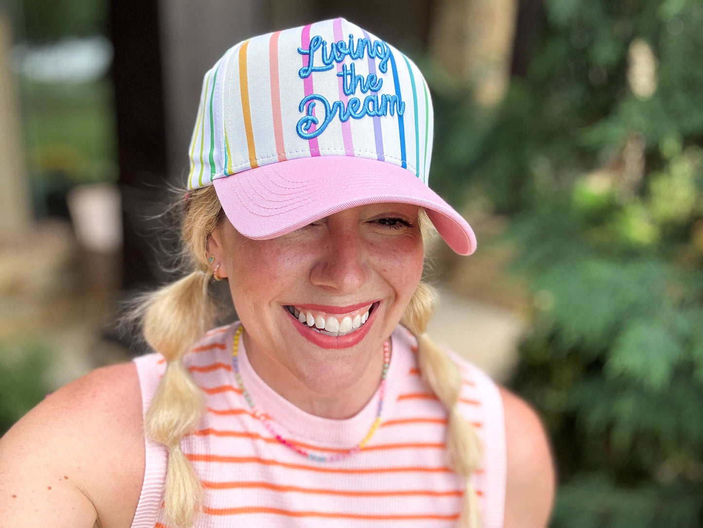 Person wearing a colorful cap with 'Living the Dream' text, smiling outdoors.