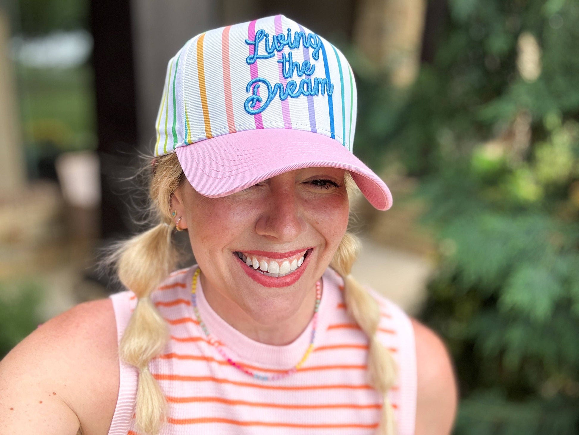 Person wearing a colorful cap with 'Living the Dream' text, smiling outdoors.