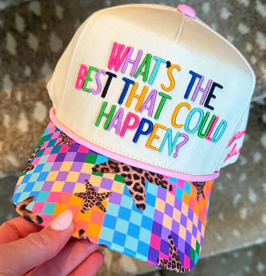 A hand holds a novelty baseball cap with a cream-colored crown and a bright multicolor brim featuring a checkered pattern, leopard print, and starfish motifs. The front of the cap has colorful embroidered text that reads 'WHAT'S THE BEST THAT COULD HAPPEN?'.