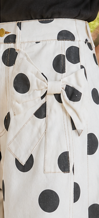 Woman wearing polka dot barrel jeans with bow pockets, standing outdoors.
