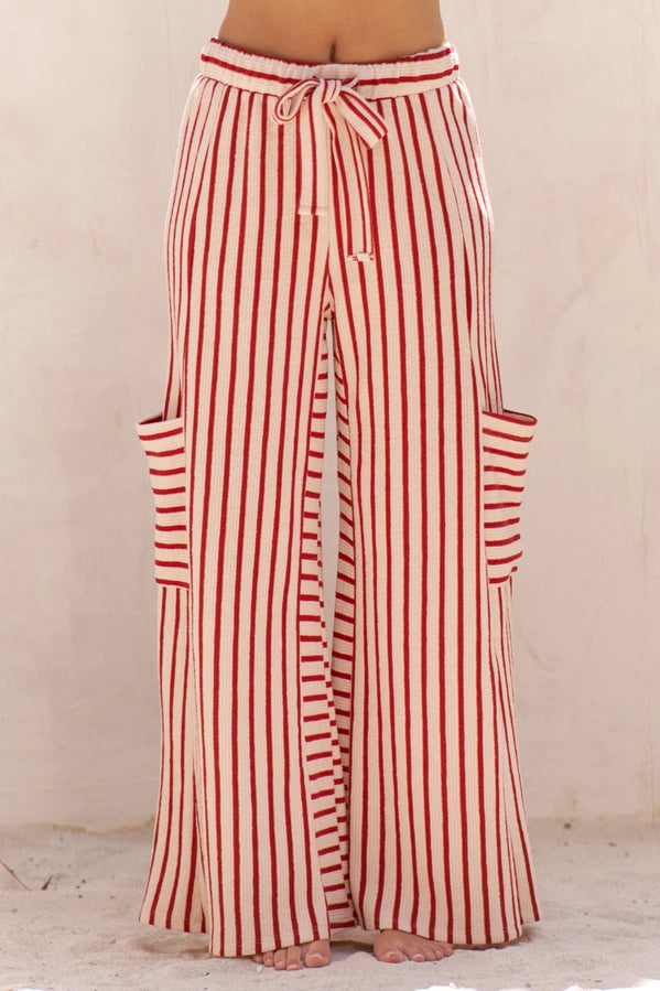 Red and cream vertical striped wide-leg pants with a drawstring waist and side pockets, shown on a model from the waist down against a neutral beige wall.