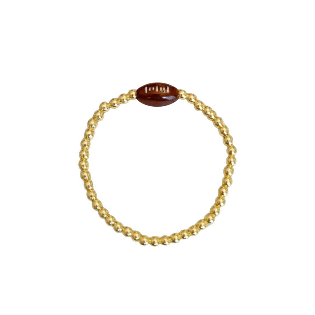 A gold beaded stretch bracelet featuring a small brown football charm set against a plain white background.