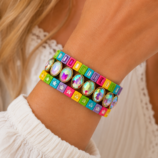 Colorful gemstone and neon stack bracelets worn on a model’s wrist with gold accents and iridescent stones.