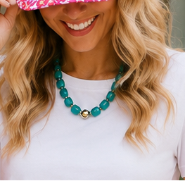 Woman wearing a turquoise beaded necklace with a white top and pink headband.