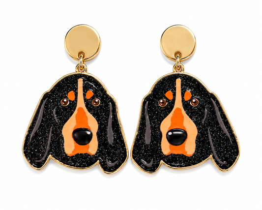 A pair of gold-tone stud earrings featuring a black and orange dog face design with glittery black ears and a smooth orange snout, shown on a plain white background.