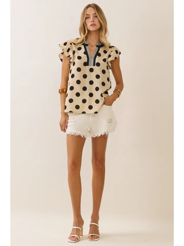 Woman wearing a polka dot top and white shorts on a plain background