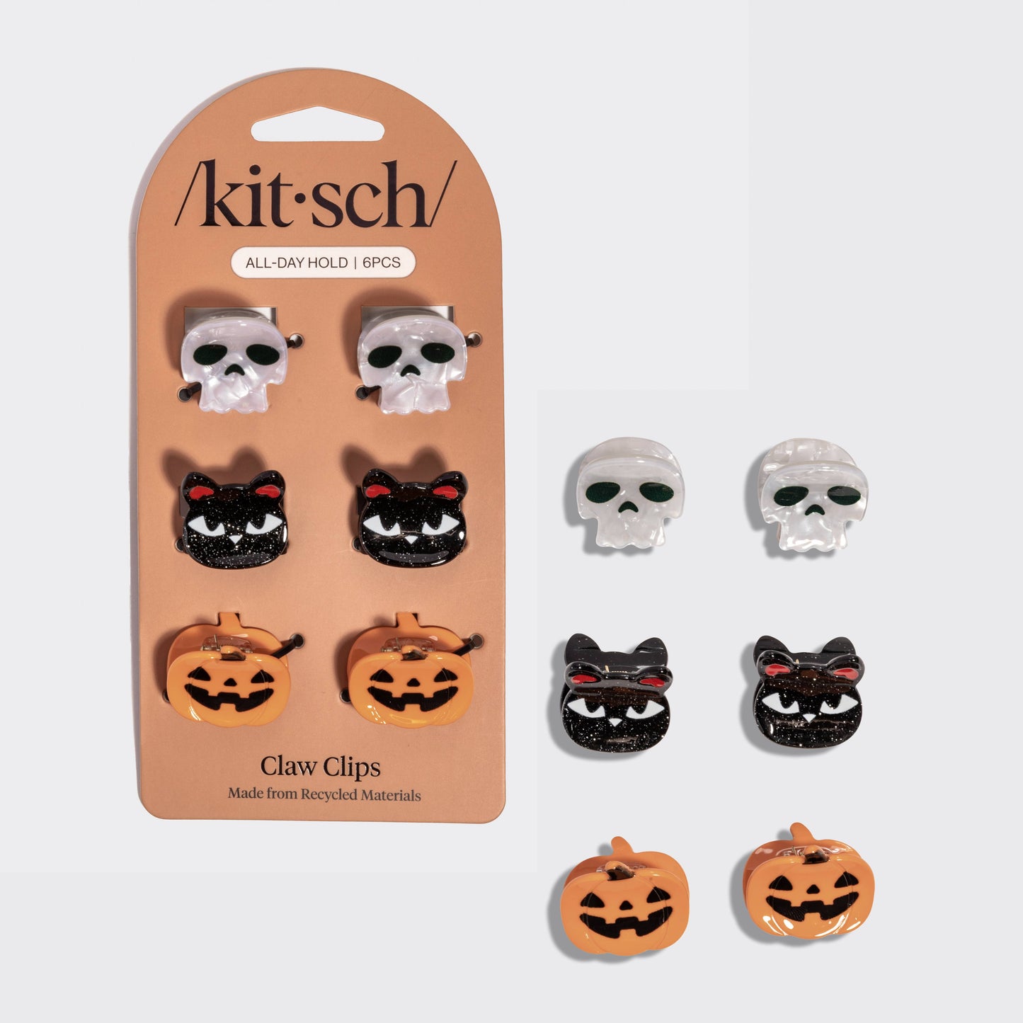 A set of Kit Sch claw clips displayed on their original peach-colored blister card alongside six loose clips. The set includes skull, black cat, and orange pumpkin designs.