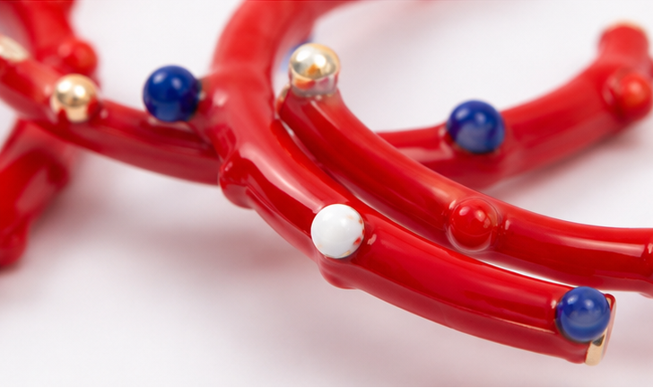 Red hoop earrings with blue and gold accents on a white background, worn by a person.