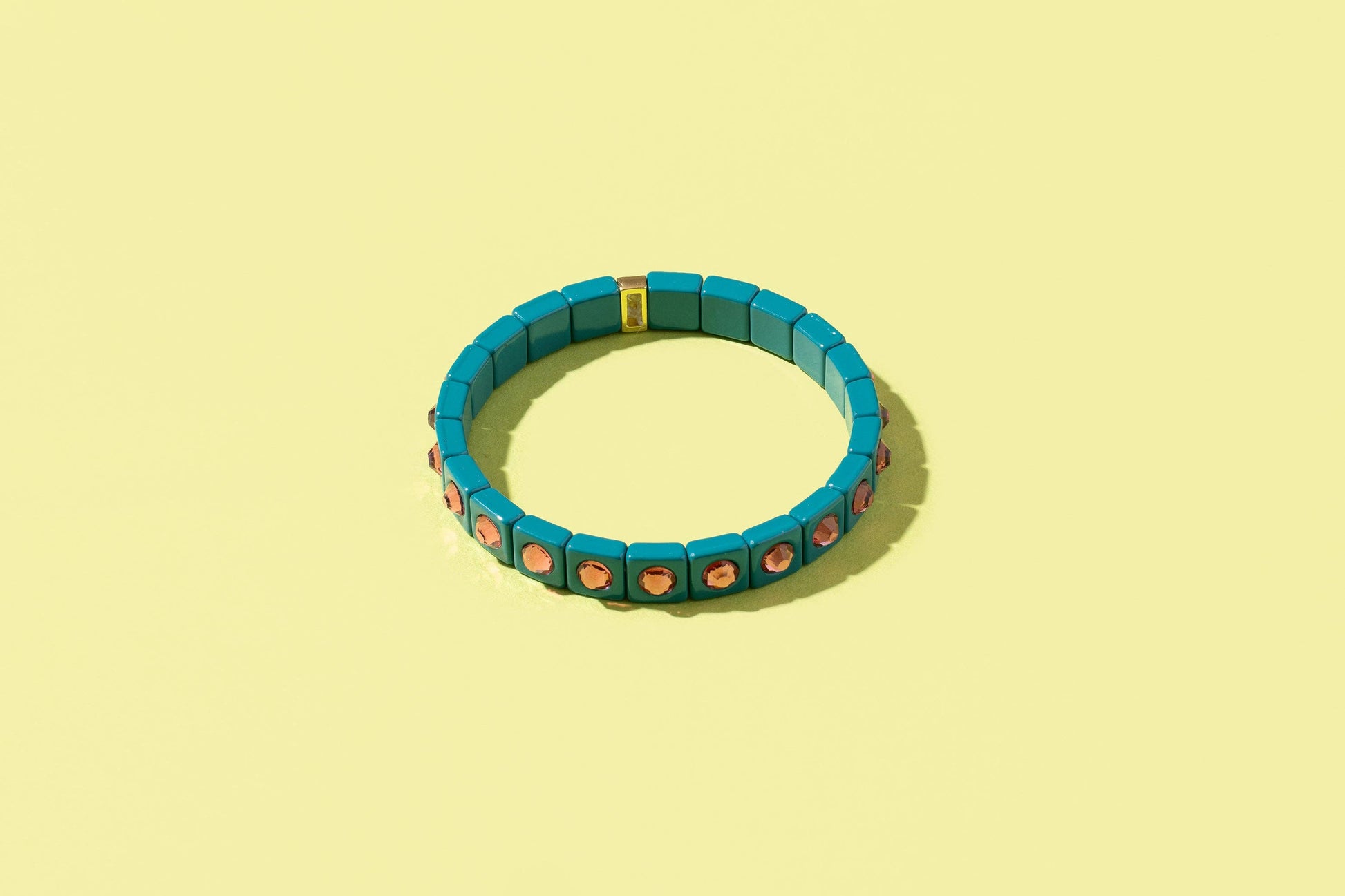 Teal bracelet with red and gold accents on a yellow background