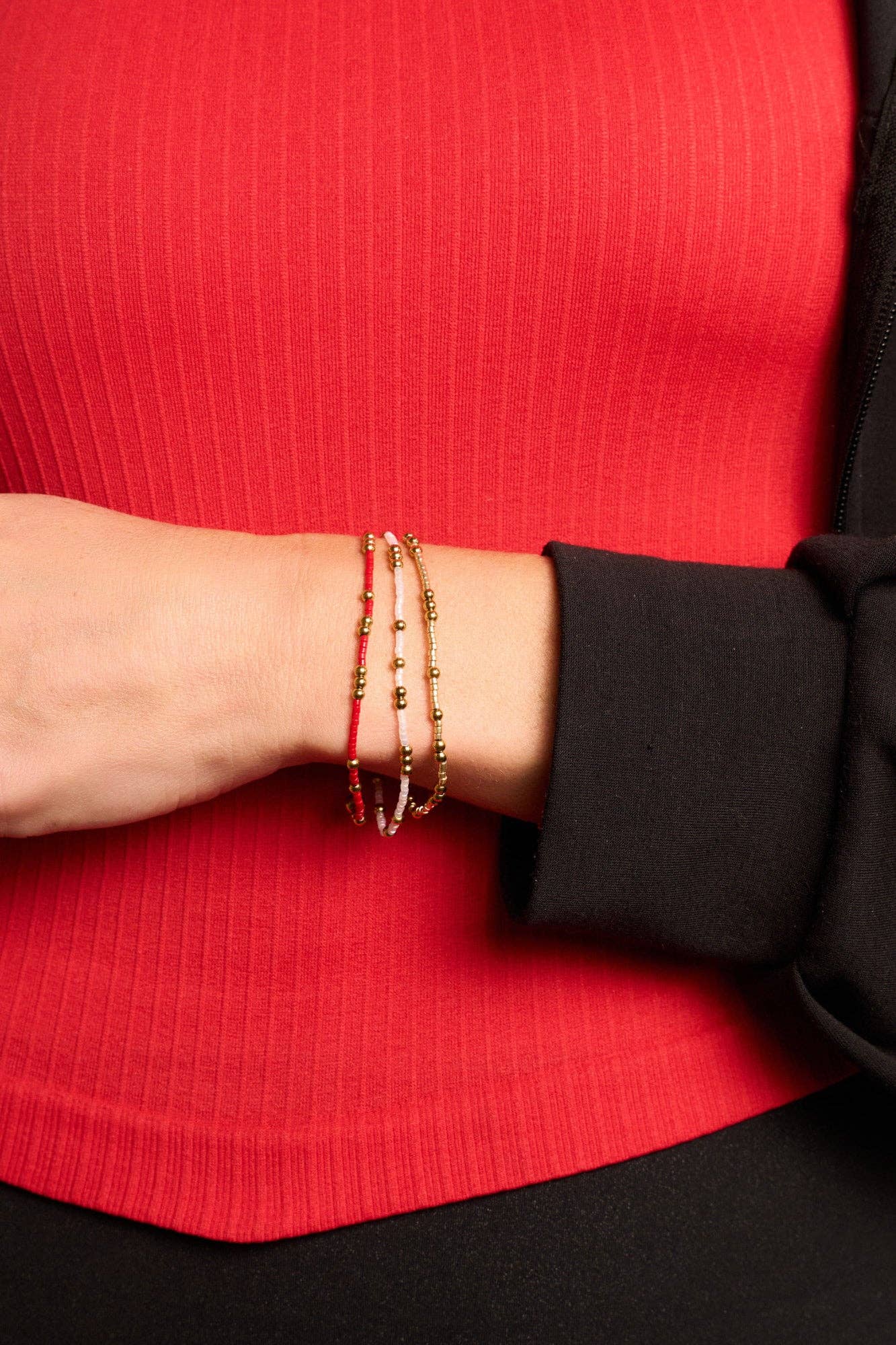 Close-up of a person wearing gold bracelets on a red and black background