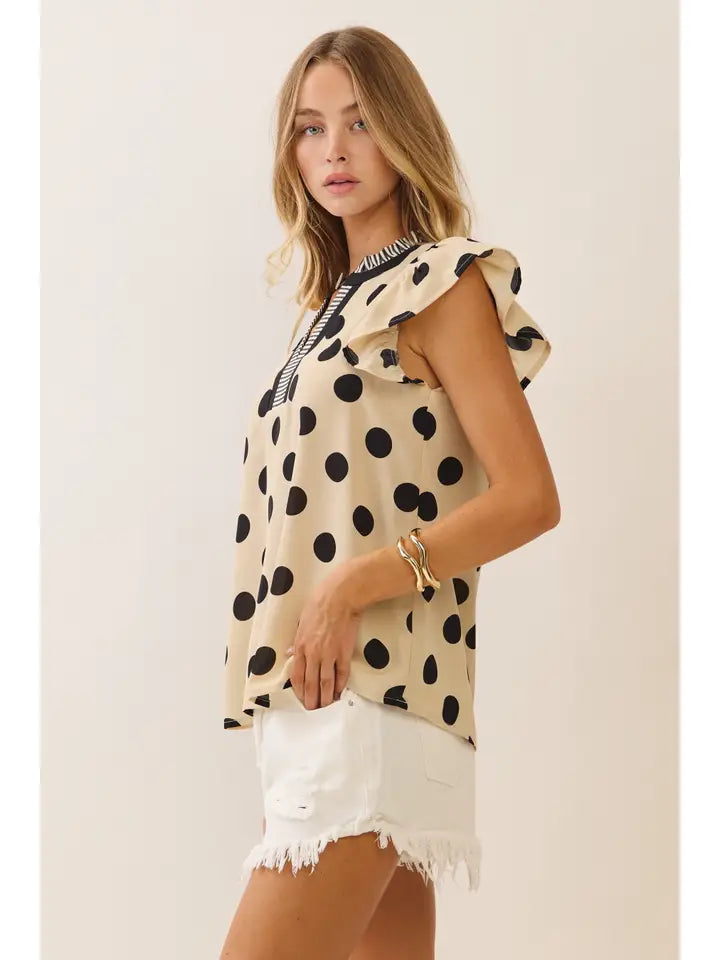 Woman wearing a polka dot top and white shorts against a plain background