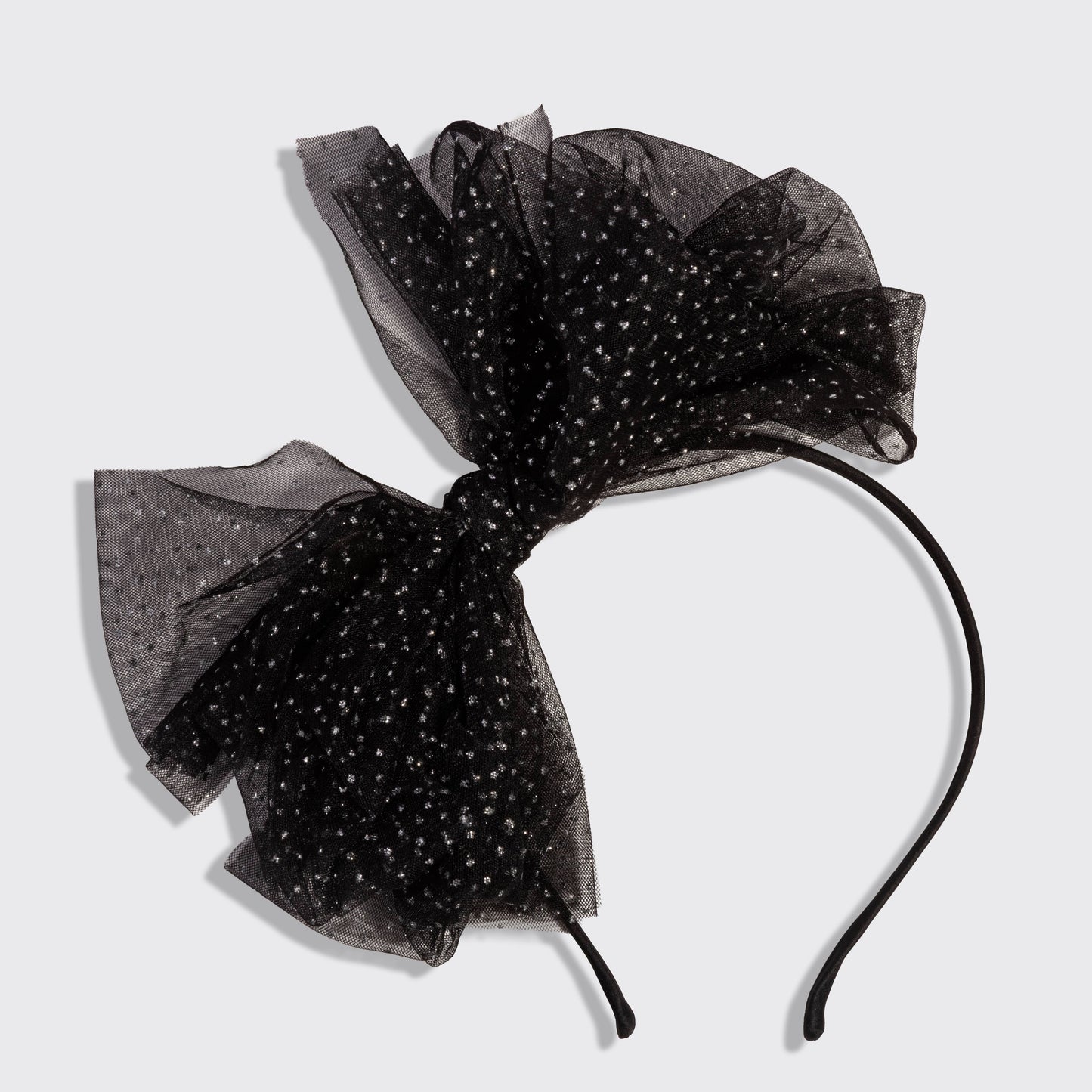 A black sheer tulle bow headband decorated with tiny white polka dots, featuring a black elastic band.