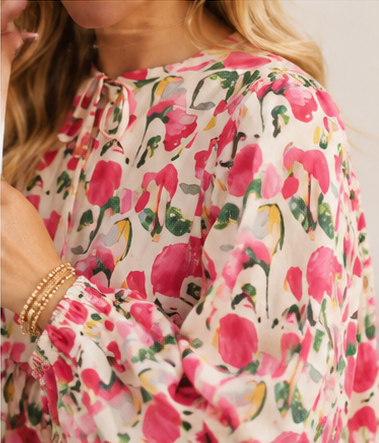 Close-up of a person wearing a floral blouse with pink flowers and green leaves.