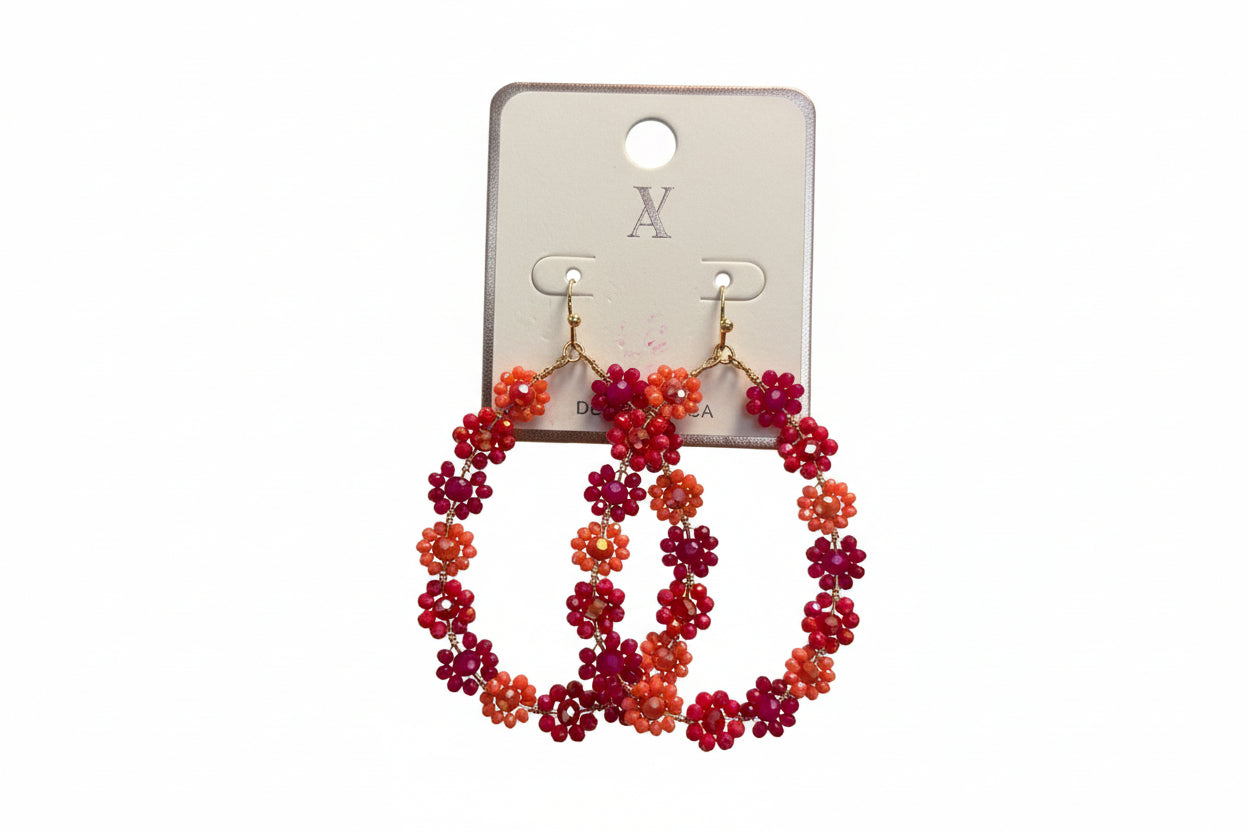 Hand holding a pair of floral earrings on a display card against a neutral background