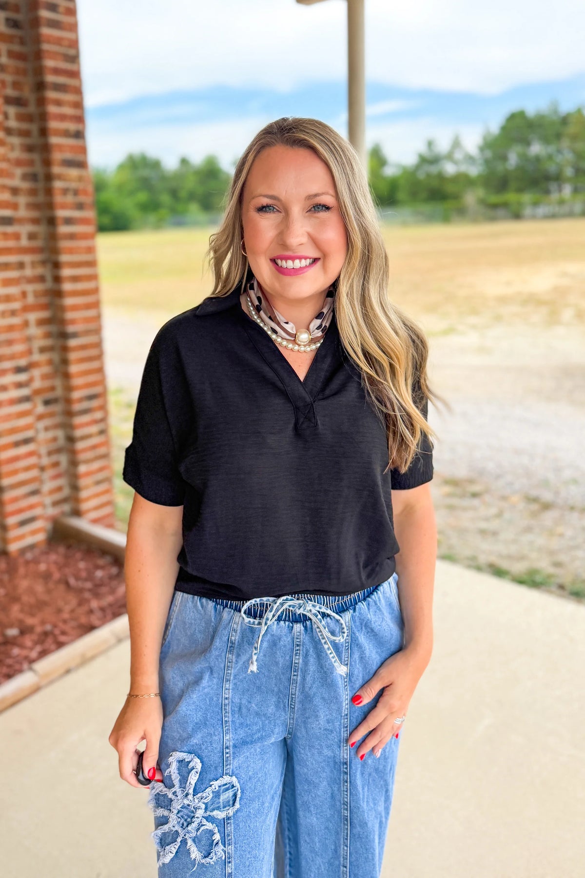 Woman wearing a zenana black top and blue jeans with floral embroidery outdoors.