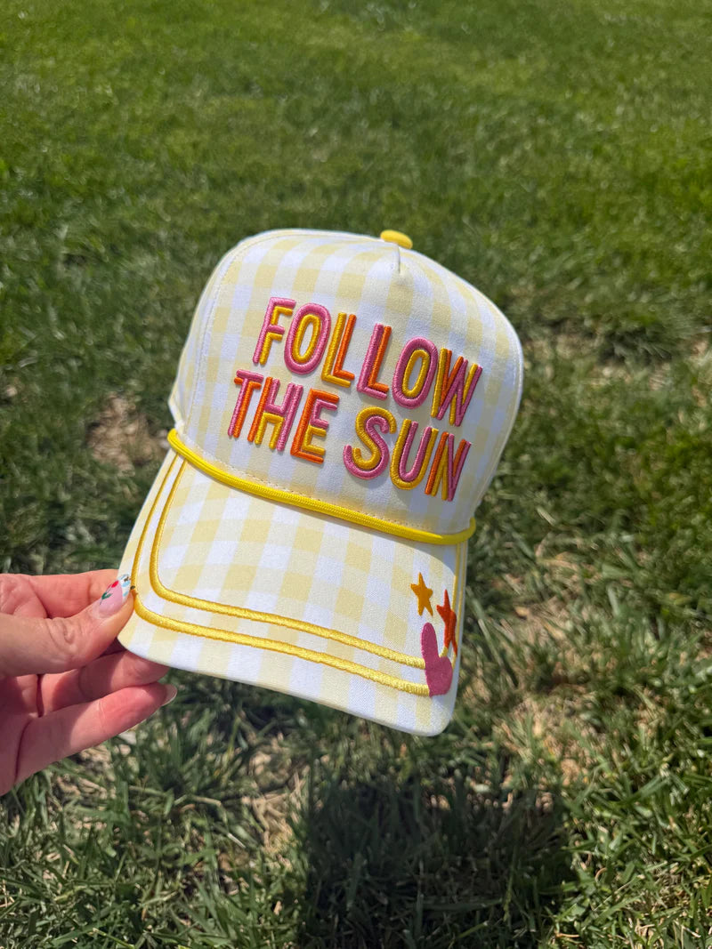 Checkered cap with 'Follow the Sun' text held in front of grass