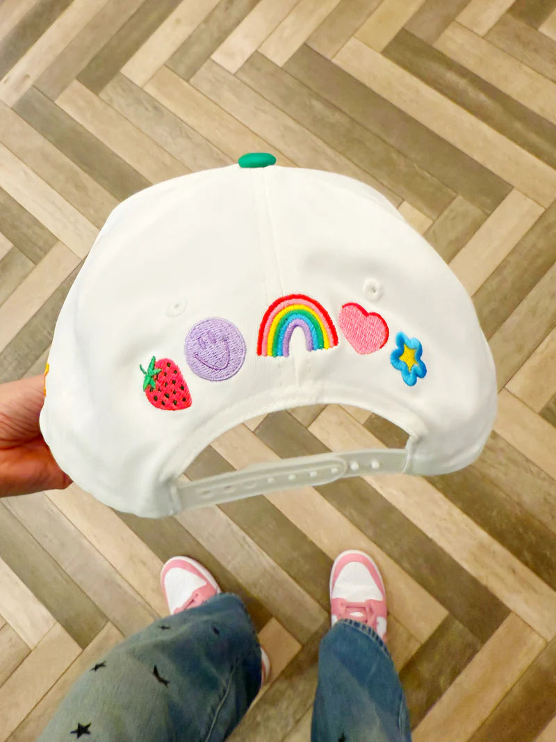 White cap with colorful decorations held by a person on a wooden floor.