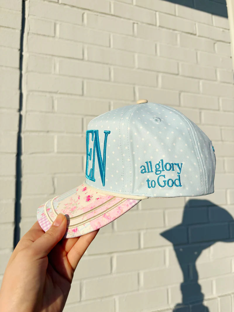 Cap with 'EN' and 'all glory to God' text held against a brick wall.