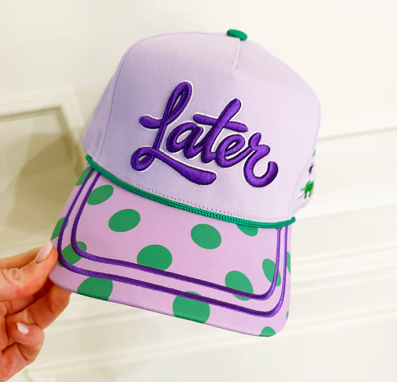 Purple cap with green polka dots and 'Later' text held by a hand on a white background