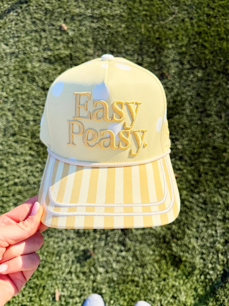 Yellow and white striped cap with 'Easy Peasy' text held against a grass background