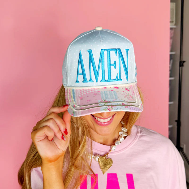 Person wearing a cap with 'AMEN' on a pink background