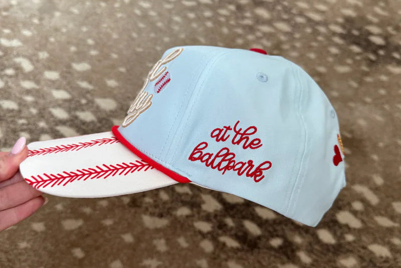 Light blue baseball cap with red stitching and text held on a patterned surface