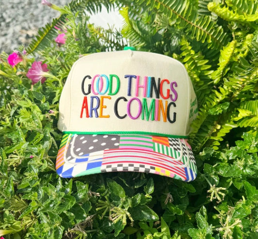 Colorful cap with 'Good Things Are Coming' text on a green leafy background