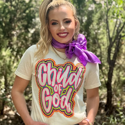 Woman wearing a cream Texas True Threads Child of God Christian graphic T-shirt with colorful retro lettering.