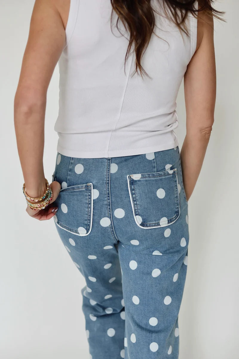 Person wearing a white sleeveless top and blue jeans with white polka dots on a plain background