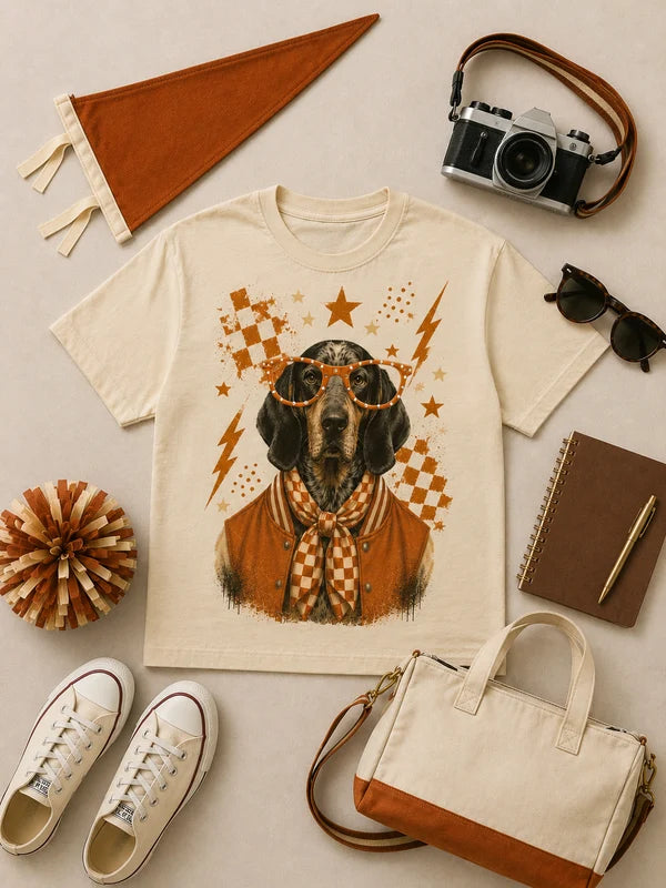 Beige t-shirt with a dog graphic surrounded by accessories on a light gray background