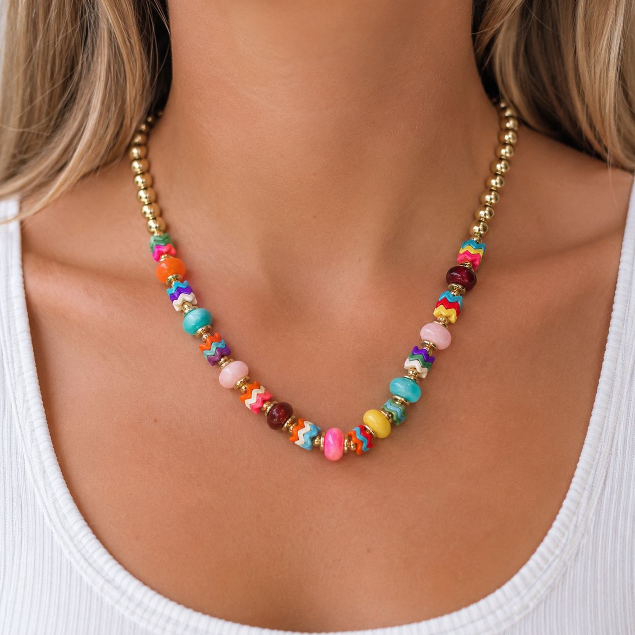 Colorful beaded statement necklace with gold accents worn on a model in a white tank top.