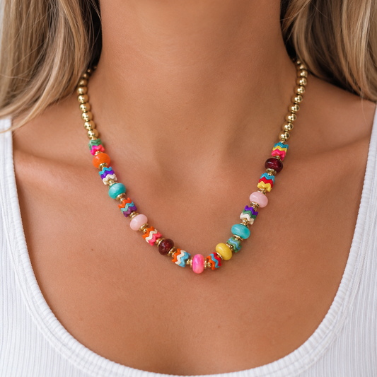 Colorful beaded statement necklace with gold accents worn on a model in a white tank top.