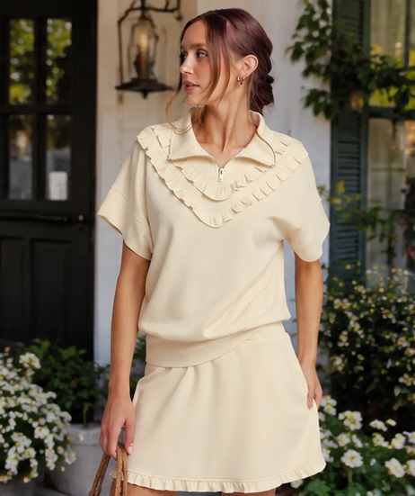 Woman wearing a cream-colored outfit with ruffled details in an outdoor setting.