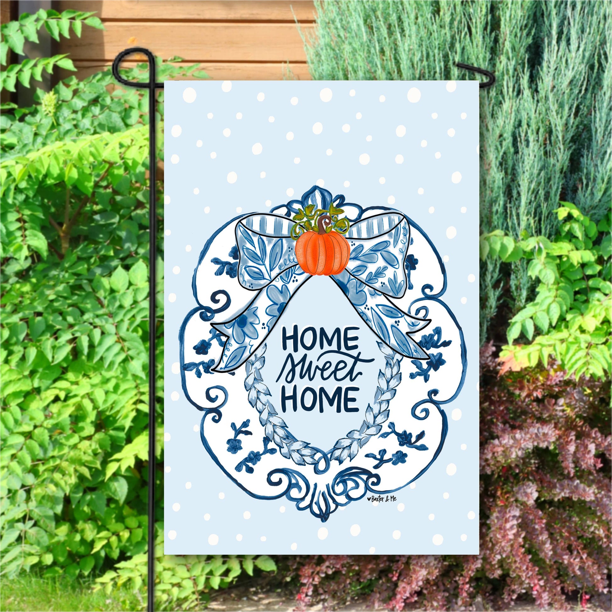 Decorative garden flag with 'Home Sweet Home' text and pumpkin design, set against a garden background.