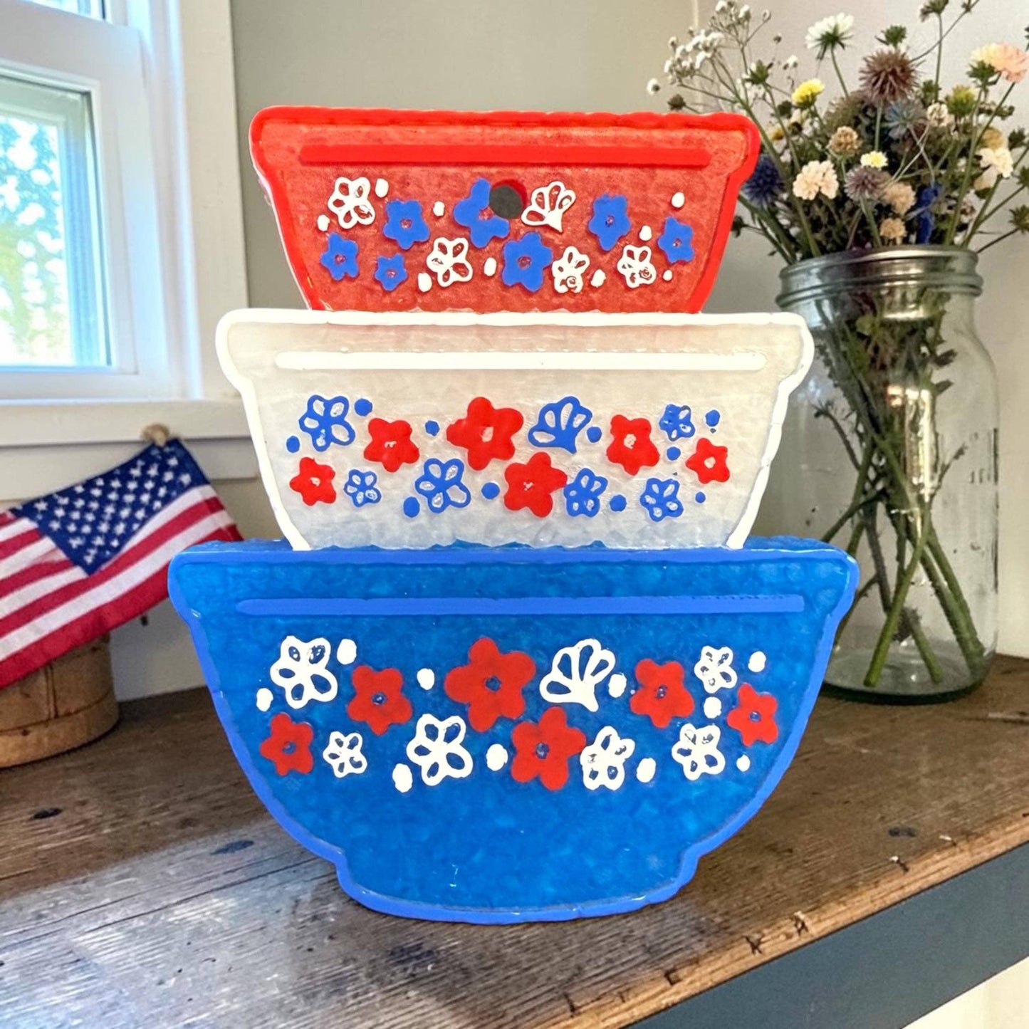 Stack of colorful floral-patterned bowls on a wooden surface with an American flag in the background.