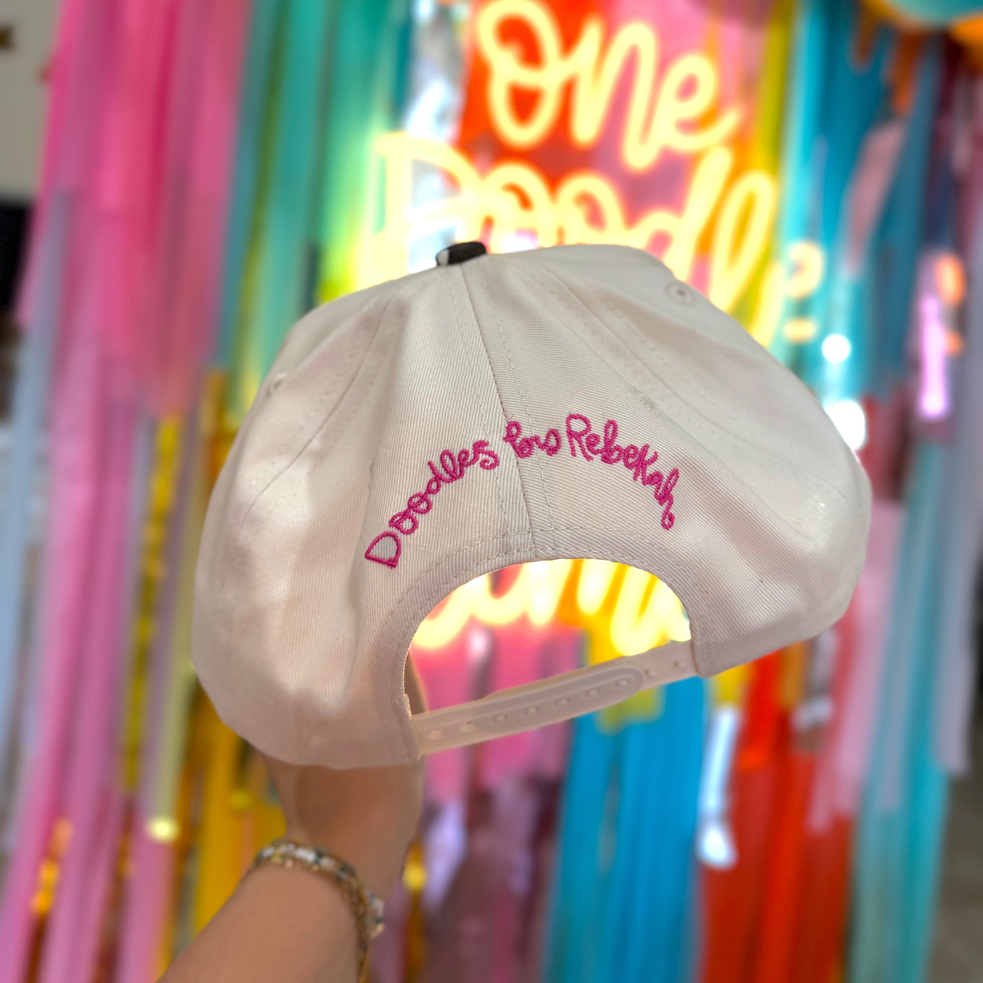 Beige cap with pink text against a colorful, neon-lit background