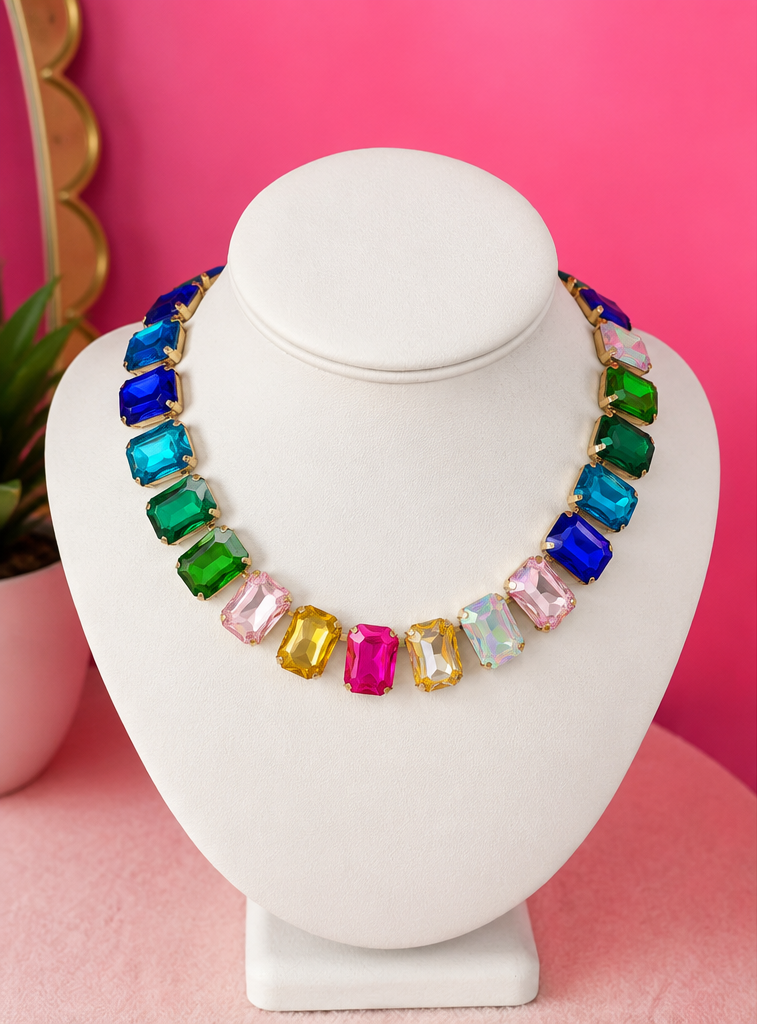 A statement colorful gemstone necklace on a white display bust against a hot pink background.