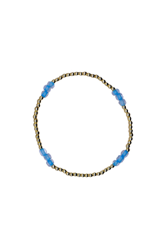 A delicate beaded bracelet with a gold-toned twisted wire base and small translucent light blue beads spaced along the top, shown on a plain white background.