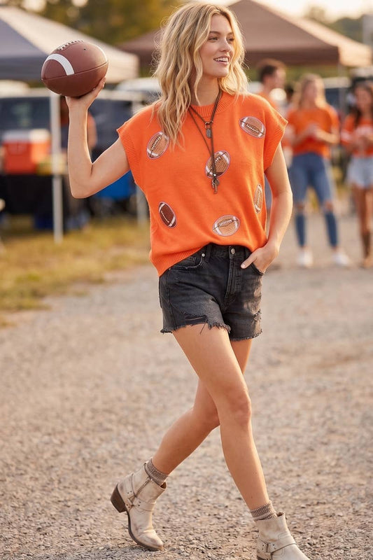 Woman wearing an orange lightweight sweater top featuring football patch appliqués with black shorts.