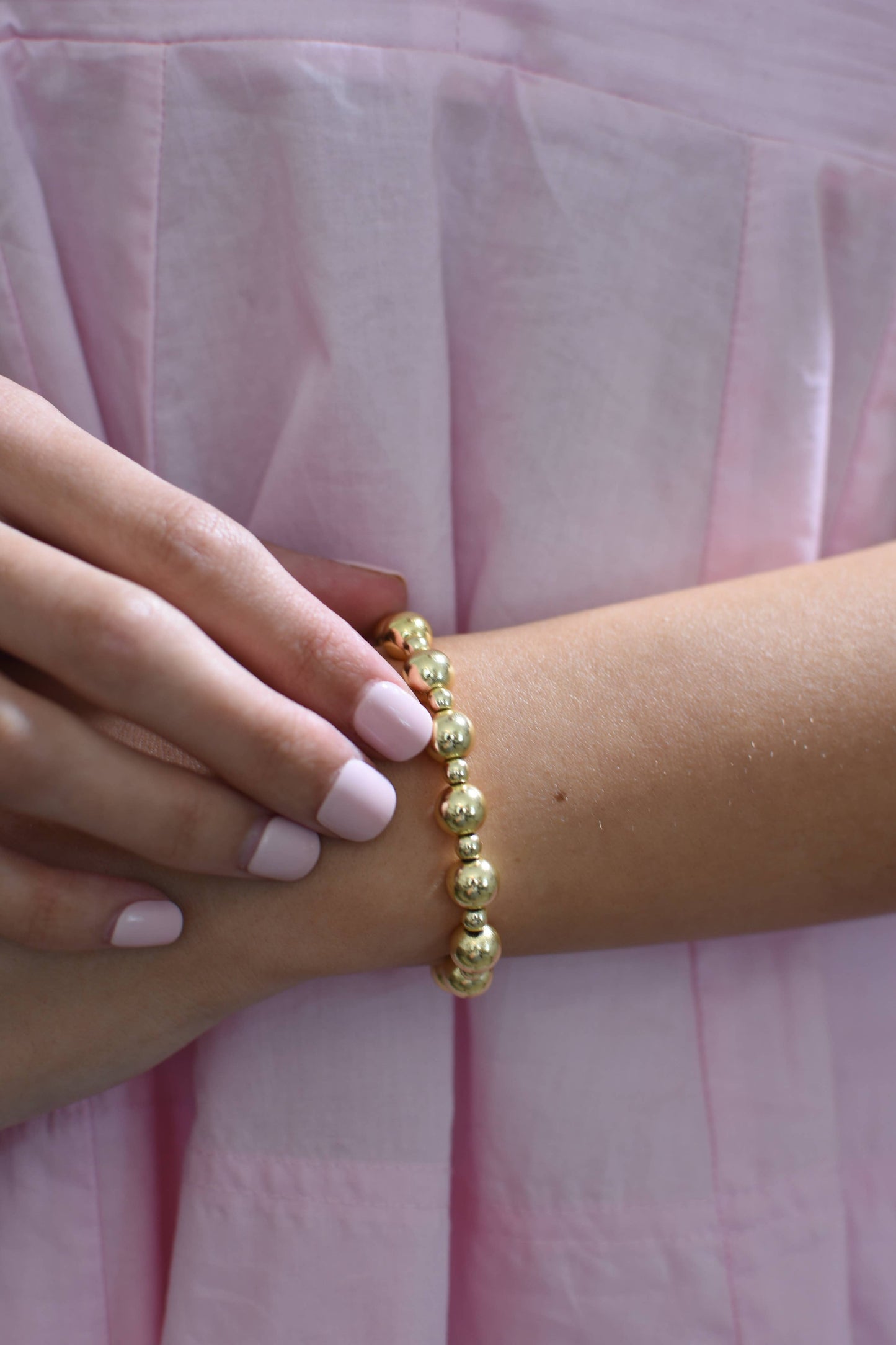 Gold beaded bracelet on a wrist with pink fabric background