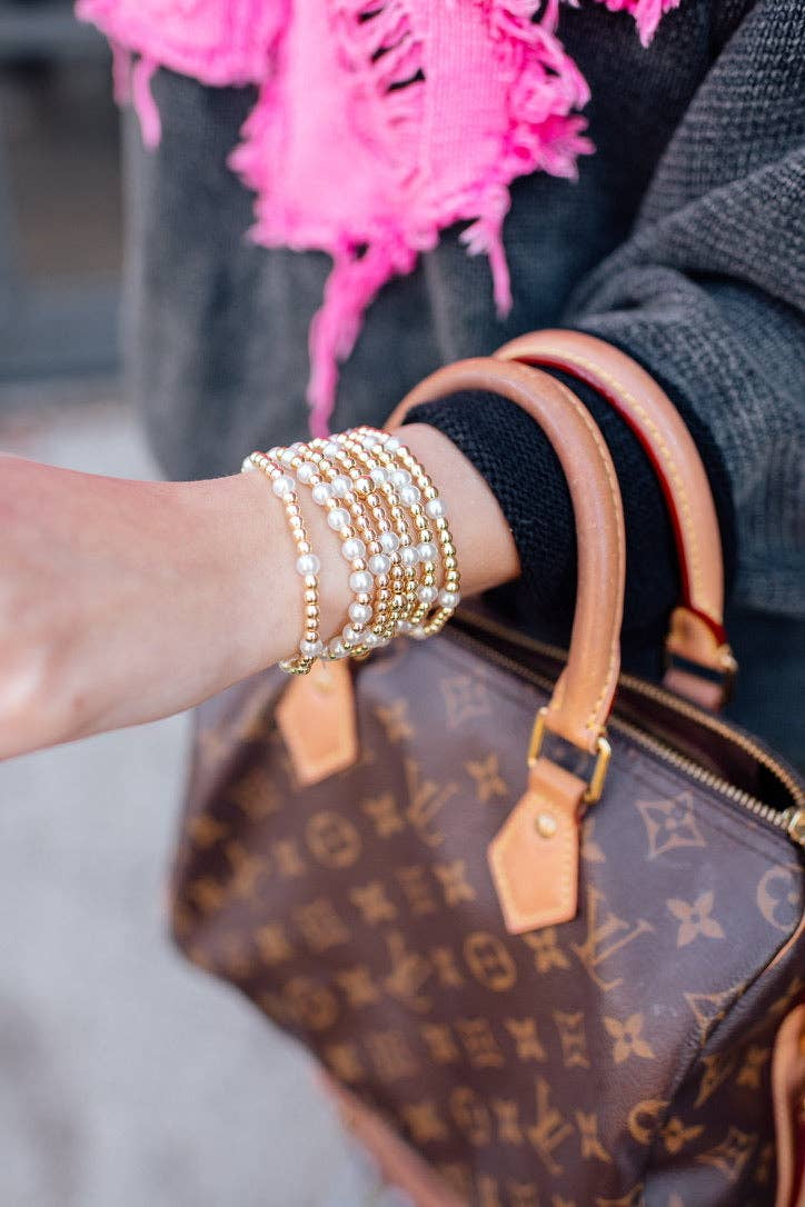 Close-up of a hand with gold bracelets holding a brown patterned handbag.