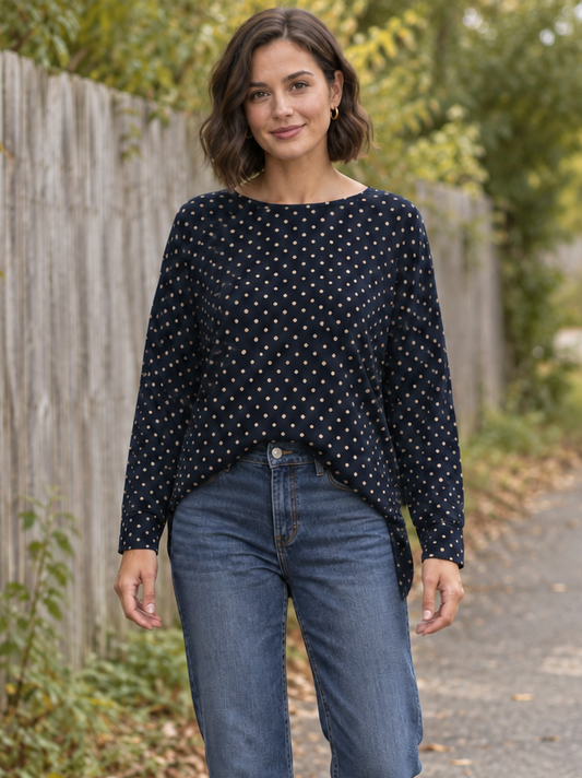 a navy and cream polka dot top with jean on a model outside by a fence. 
