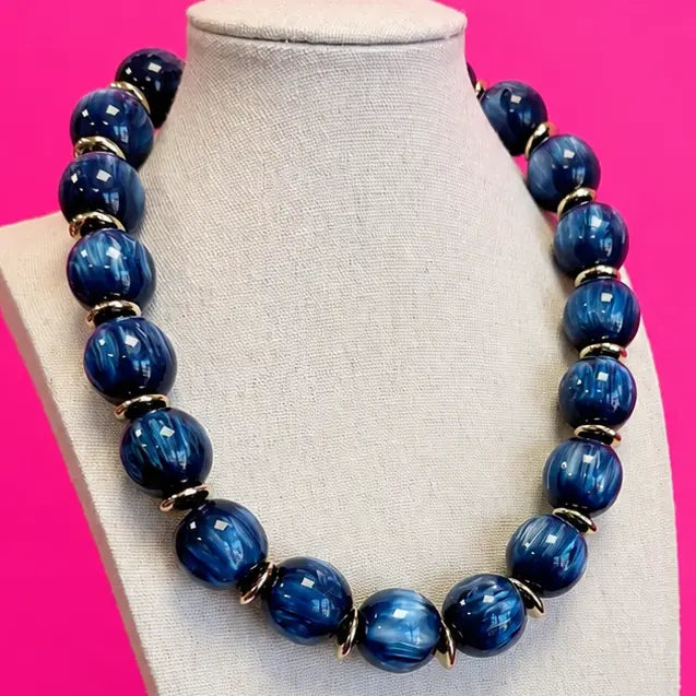 Navy blue marbled statement bead necklace with gold-tone spacer accents, displayed on a jewelry bust.