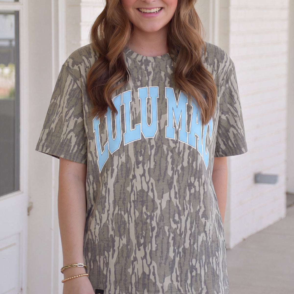 Woman wearing Lulu Mac Mossy Oak Bottomland camo tee with light blue Lulu Mac lettering