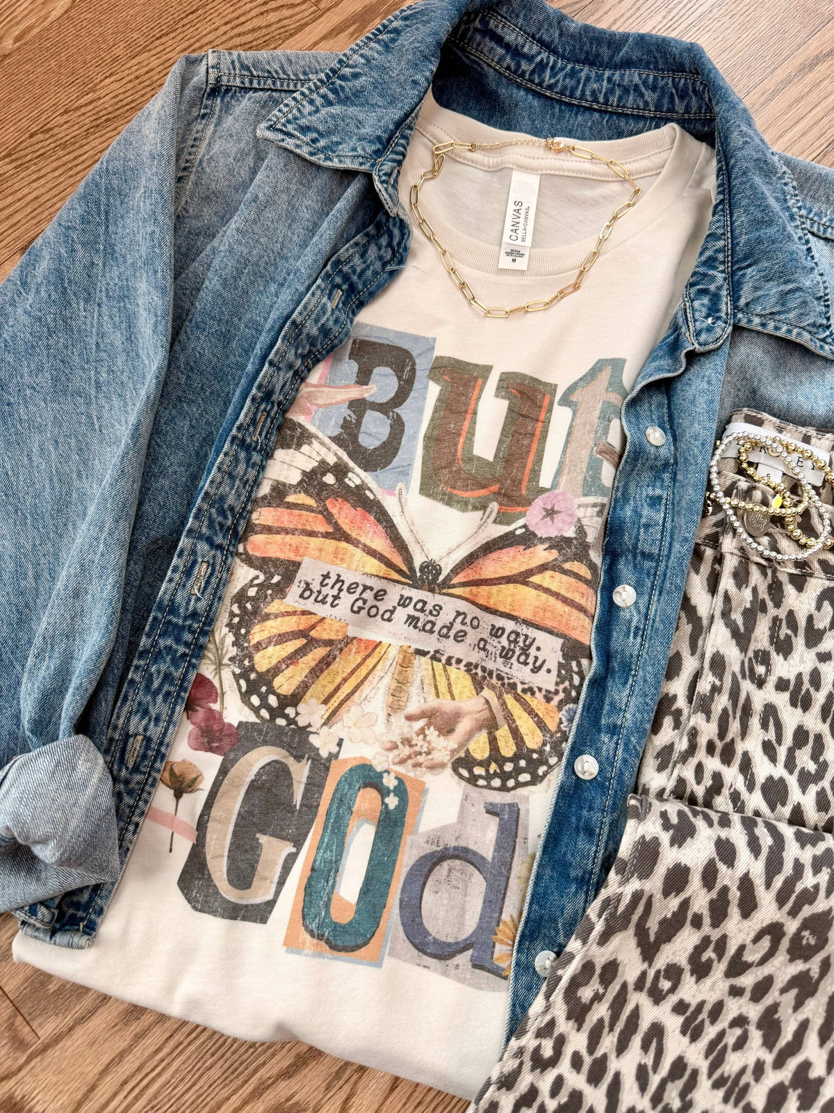 T-shirt with butterfly design and text layered under a denim jacket on a wooden surface