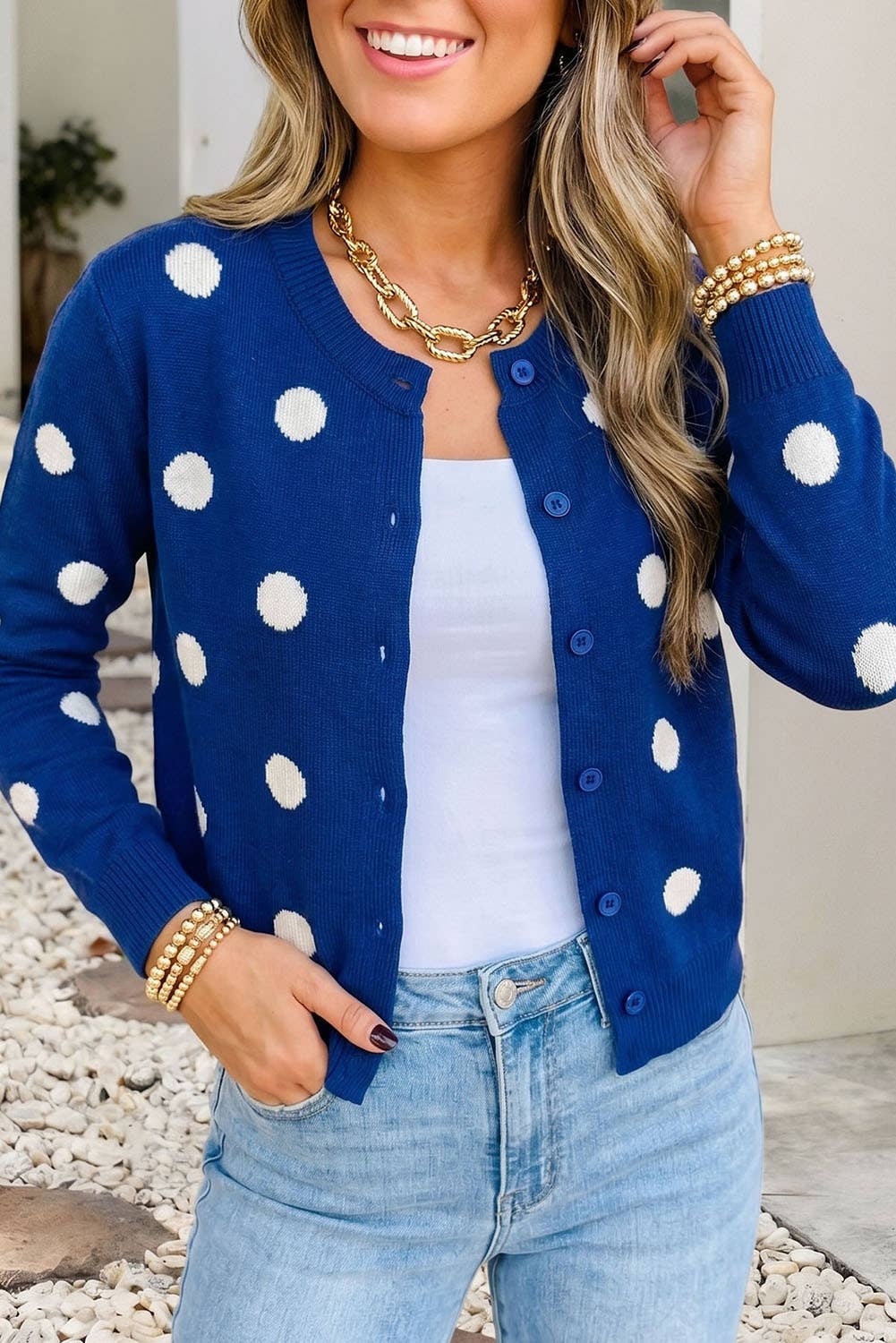 Woman wearing a blue cardigan with white polka dots, white top, and light blue jeans.
